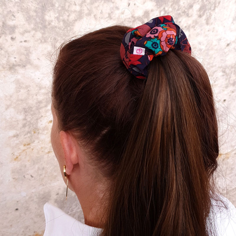 une femme a attaché ses cheveux en une queue de cheval avec un chouchou automnal violet profond à fleurs colorées de taille médium de la marque Bunzelle