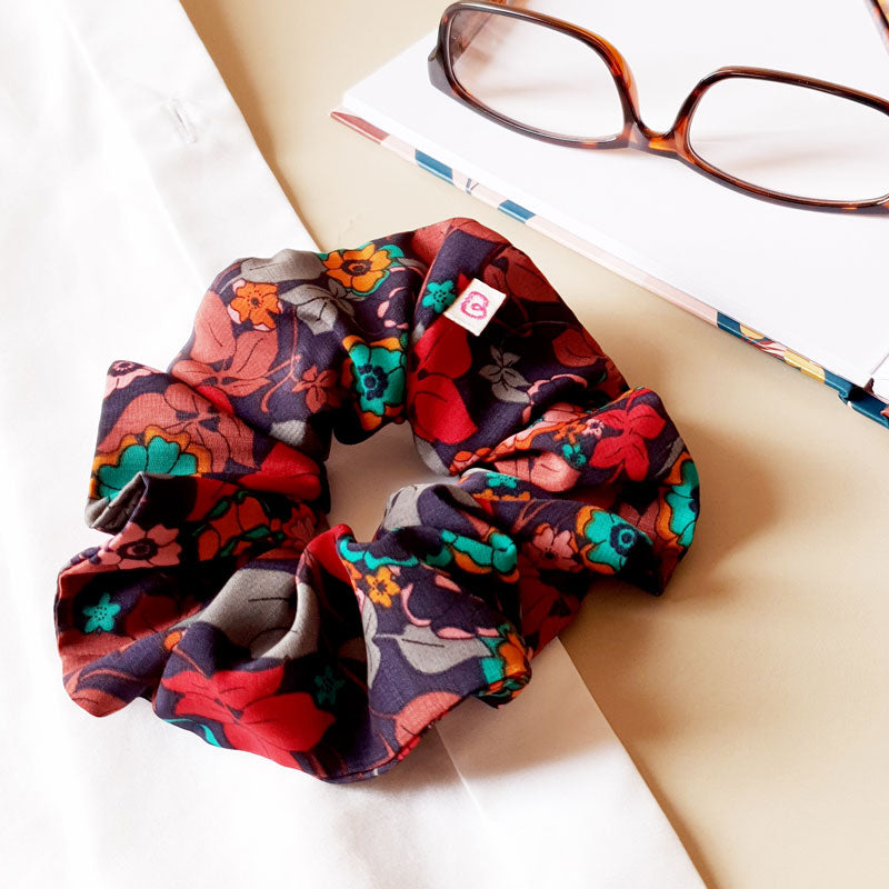 un maxi chouchou cheveux automnal, violet profond à fleurs colorées de la marque Bunzelle est posé à côté d'une paire de lunettes