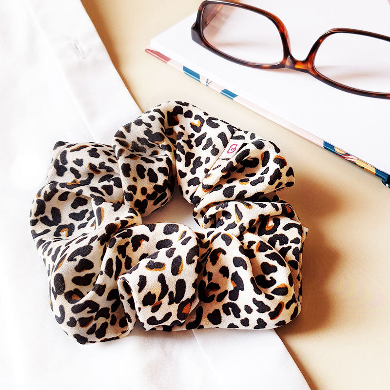un chouchou pour cheveux léopard de la marque Bunzelle est posé à côté d'une paire de lunettes