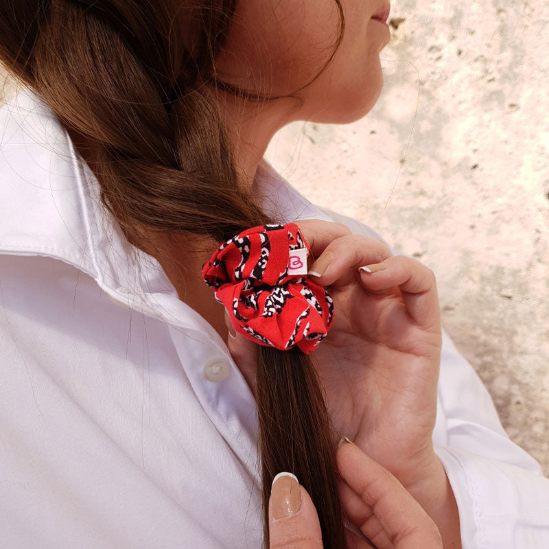 une femme a attachée sa tresse de cheveux avec un mini chouchou rouge à motif zèbre de la marque Bunzelle